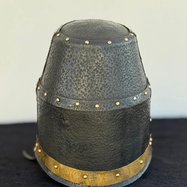May include: A black helmet with a textured surface and gold accents. The helmet has a band of gold around the bottom with a repeating pattern of four-leaf clover designs.