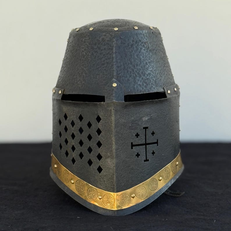 May include: A black metal helmet with a gold trim and a cross design. The helmet has a visor and a series of holes on the front.