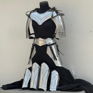 May include: A silver-colored metal armor set for LARP or cosplay. The set includes a chest piece, shoulder pads, a belt, leg guards, and shin guards.