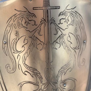 May include: A gold shield with two dragons facing each other, their tails intertwined. A sword is centered between the dragons, with the hilt at the top of the shield.