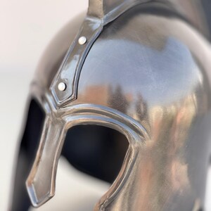 May include: A black metal helmet with a pointed crest and a visor. The helmet has a smooth, polished finish and is decorated with small metal rivets.