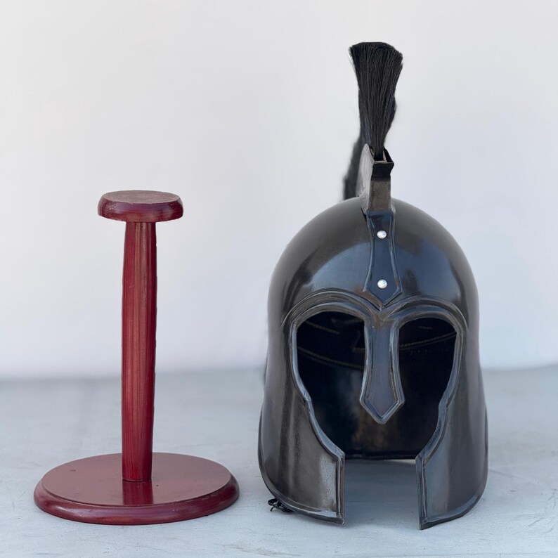 May include: A black metal helmet with a black horsehair plume on top. The helmet is on a wooden stand with a red finish.