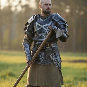 May include: A person in medieval armour, holding a large axe. The armour combines metal plates and chainmail, with a brown skirt and tall black boots. The background is a field of green grass.