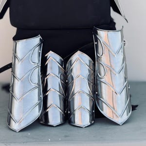 K&ouml;nnte beinhalten: Vier silberne Armstulpen aus Metall mit einem dekorativen Design. Die Stulpen sind aus Metall und haben eine gl&auml;nzende Oberfl&auml;che.