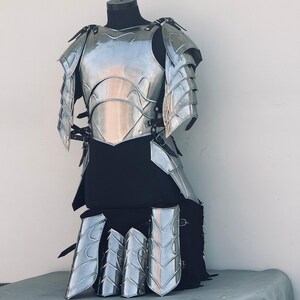 K&ouml;nnte beinhalten: Ein silberfarbener Metall-R&uuml;stungsset mit Brustpanzer, Schulterpolstern und Beinschienen. Die R&uuml;stung hat ein dekoratives Design mit einem schuppigen Muster.