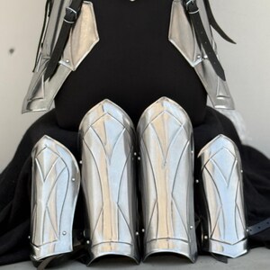May include: Set of five silver-colored metal arm guards with a decorative design. The guards are made of metal and have a shiny finish.