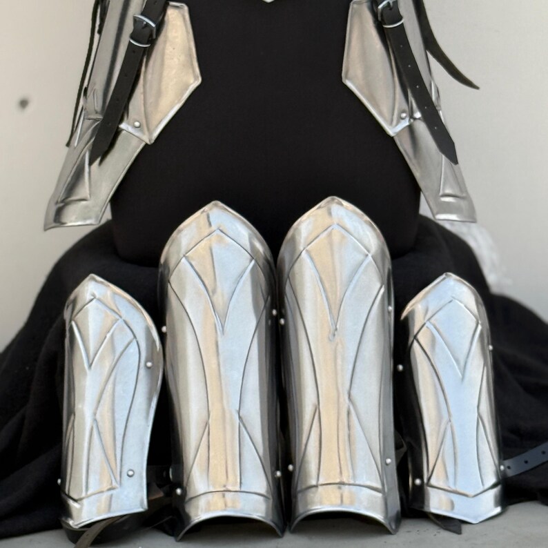 May include: Set of five silver-colored metal arm guards with a decorative design. The guards are made of metal and have a shiny finish.