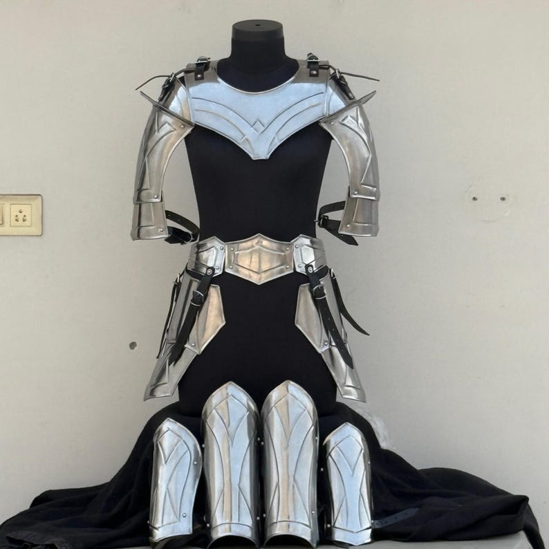 May include: A silver-colored armor set with a breastplate, shoulder pads, leg guards, and a belt. The armor is displayed on a black mannequin.