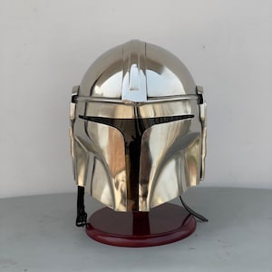 May include: A silver Mandalorian helmet with a visor and a dark brown wooden stand.