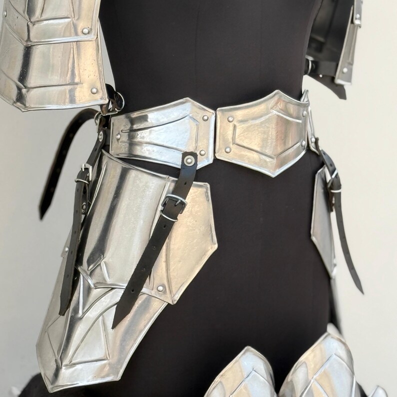 May include: Silver plated armor with black leather straps. The armor includes a breastplate, shoulder pads, and leg guards.