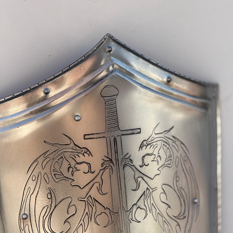May include: A silver metal shield with a sword and two dragons etched into the surface.