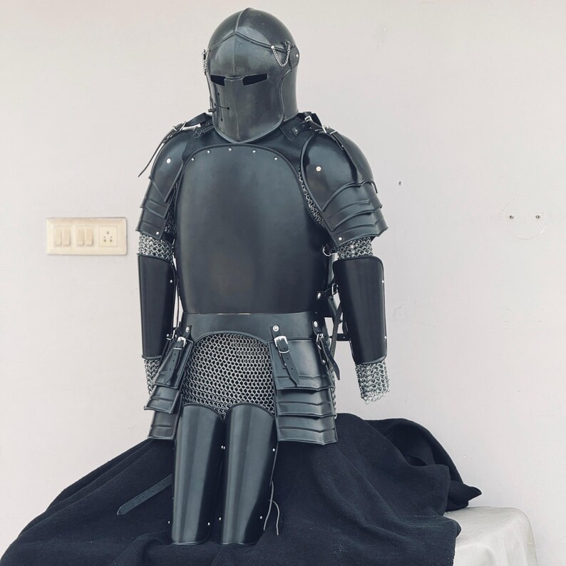 May include: A full suit of black armor with a helmet, chainmail, and plate armor. The armor is displayed on a black cloth background.