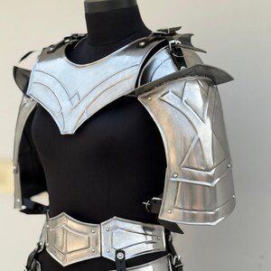 May include: Silver-toned metal armor for the chest and shoulders. The armor has a decorative design with a pointed collar and a belt.