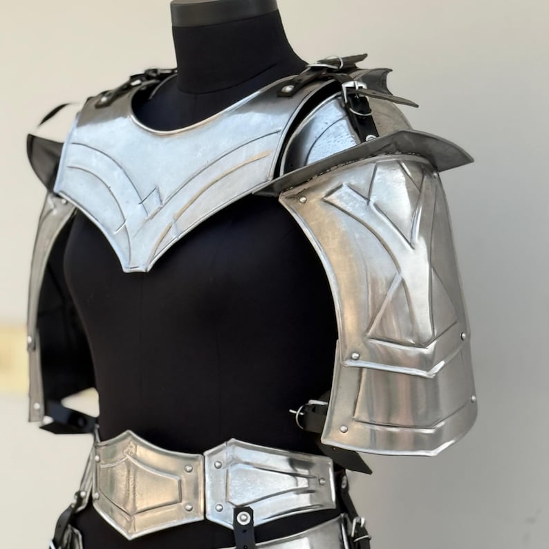 May include: Silver-toned metal armor for the chest and shoulders. The armor has a decorative design with a pointed collar and a belt.