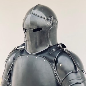May include: A black metal helmet with a visor and chainmail accents. The helmet is part of a suit of armor, which includes a black metal breastplate and shoulder pads.