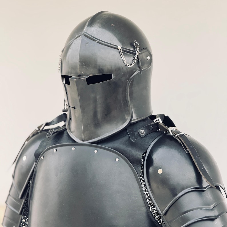 May include: A black metal helmet with a visor and chainmail accents. The helmet is part of a suit of armor, which includes a black metal breastplate and shoulder pads.