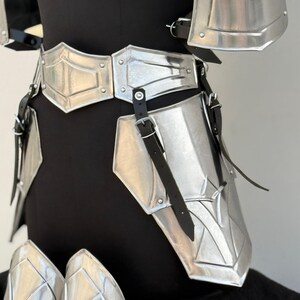 May include: Silver metal armor for the legs and waist with black leather straps. The armor is made up of multiple plates that are connected together.