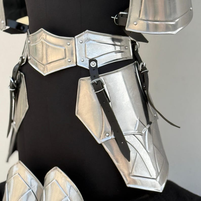 May include: Silver metal armor for the legs and waist with black leather straps. The armor is made up of multiple plates that are connected together.