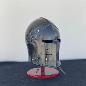 May include: A black helmet with a visor and a chain detail. The helmet is on a red stand.