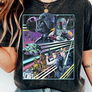 Könnte beinhalten: Ein schwarzes T-Shirt mit einer Grafik im Vintage-Stil von Star Wars-Charakteren, darunter Darth Vader, Boba Fett, Chewbacca, C-3PO und R2-D2. Die Grafik ist vor dem Hintergrund einer Galaxie mit Sternen und Planeten platziert.