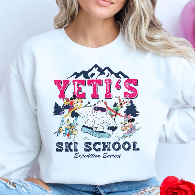 May include: White sweatshirt with a graphic of a Yeti and Mickey Mouse characters skiing. The text "YETI'S SKI SCHOOL Expedition Everest" is printed on the sweatshirt.