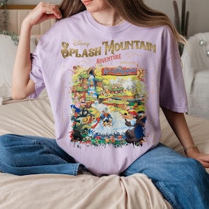 May include: A lavender t-shirt with a graphic print of a cartoon scene featuring the text "Disney Splash Mountain Adventure".