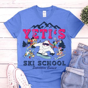 May include: A blue t-shirt with a graphic of a Yeti and Disney characters skiing. The text "YETI'S SKI SCHOOL Expedition Everest" is printed on the shirt.