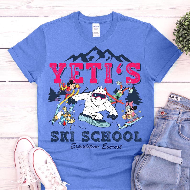 May include: A blue t-shirt with a graphic of a Yeti and Disney characters skiing. The text "YETI'S SKI SCHOOL Expedition Everest" is printed on the shirt.