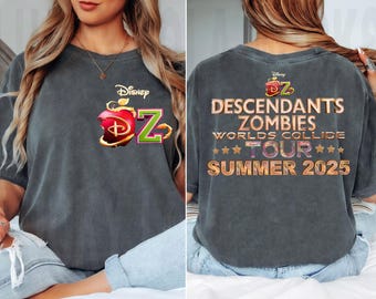 May include: Dark gray t-shirt featuring the Disney Descendants logo with a red apple and the letter "Z". The back of the shirt displays "Descendants Zombies Worlds Collide Tour Summer 2025" in gold lettering.