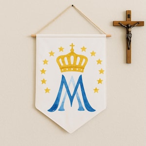 May include: White banner featuring a gold crown, blue and gold letter "M", and yellow stars. The banner is suspended on a wall beside a wooden crucifix.