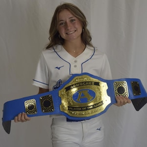 Pu&ograve; includere: Una cintura da campionato blu con una grande placca centrale dorata con il testo ARMUCHEE e PLAYER OF THE GAME, centrata con una lettera A blu. La cintura include placche laterali dorate pi&ugrave; piccole con motivi a scacchi neri.