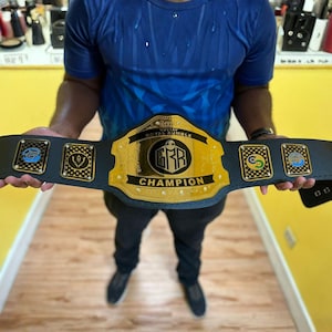 Pu&ograve; includere: Una cintura da campionato nera con una grande placca centrale dorata con il testo GUSTAV ROYAL RUMBLE CHAMPION e un logo esagonale centrale. La cintura include quattro placche laterali rettangolari pi&ugrave; piccole con emblemi circolari colorati.