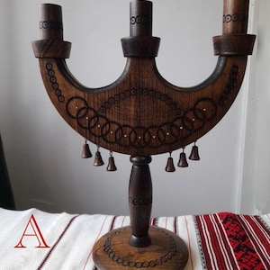 May include: A dark brown wooden candelabra with three candle holders. The candelabra has decorative etched circles and small bells hanging from the bottom. The base is round and also has etched detailing.