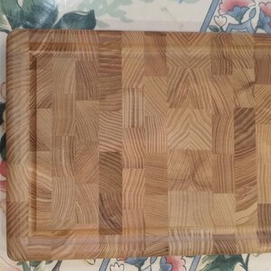 May include: A rectangular end-grain chopping board made of light brown wood. It features a recessed juice groove around the edge. The wood grain pattern is visible, creating a textured surface. This kitchen item is ideal for food preparation and measures approximately 40cm x 25cm.