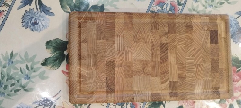 May include: A rectangular end-grain chopping board made of light brown wood. It features a recessed juice groove around the edge. The wood grain pattern is visible, creating a textured surface. This kitchen item is ideal for food preparation and measures approximately 40cm x 25cm.
