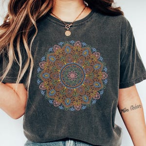 May include: A dark gray t-shirt with a colorful mandala design printed on the front. The mandala is a circular pattern with intricate details in shades of blue, pink, yellow, and orange.