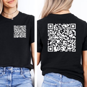 May include: Black t-shirt with a white QR code printed on the front and back. The shirt is short-sleeved and worn with blue jeans. The QR code is a square pattern of black and white squares.