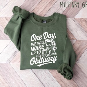 May include: A green sweatshirt with the text "One Day, We Will Wake Up To His Obituary" and a retro illustration of a woman holding a coffee cup.