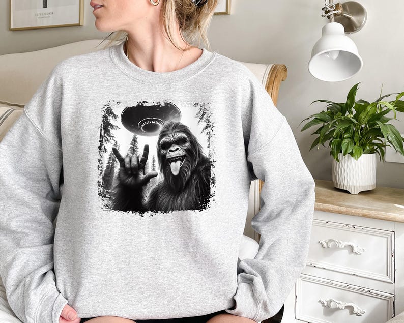 May include: Gray sweatshirt with a black and white graphic of a Bigfoot giving the peace sign with a UFO in the background.