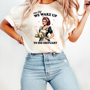 May include: A white t-shirt with a graphic of a woman in a maid outfit holding a teapot and teacups. The text on the shirt reads "one day WE WAKE UP TO HIS OBITUARY".