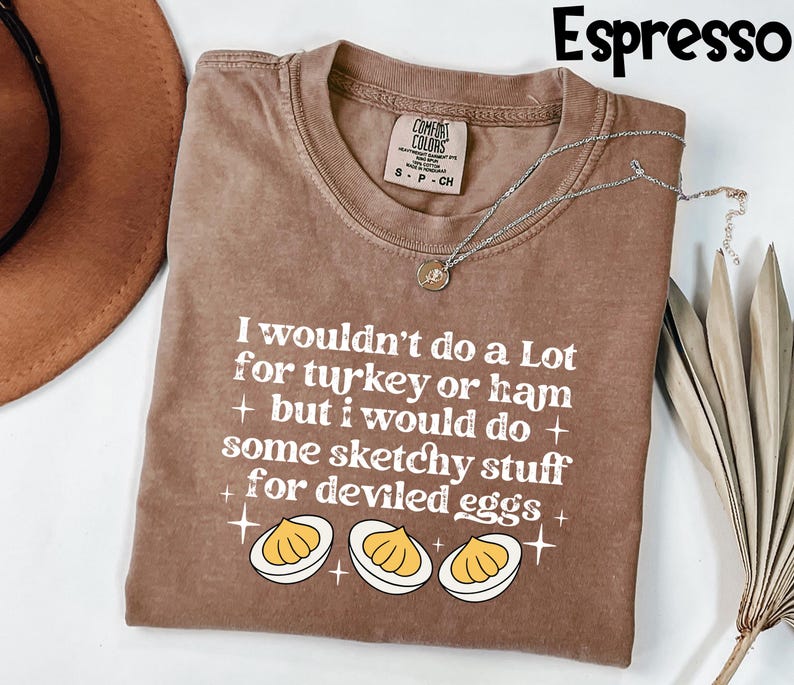 May include: Espresso-colored t-shirt with the text "I wouldn't do a Lot for turkey or ham + but I would do + some sketchy stuff + for deviled eggs +" and a graphic of deviled eggs. A silver necklace is draped across the shirt.