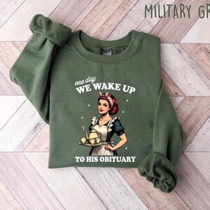 May include: Green sweatshirt with a white graphic of a woman holding a teapot and teacups. The text on the graphic reads "one day we wake up to his obituary".