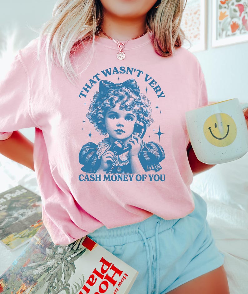 Puede incluir: Camiseta rosa con una ilustraci&oacute;n vintage de una ni&ntilde;a al tel&eacute;fono. El texto en la camiseta dice "That wasn't very cash money of you."
