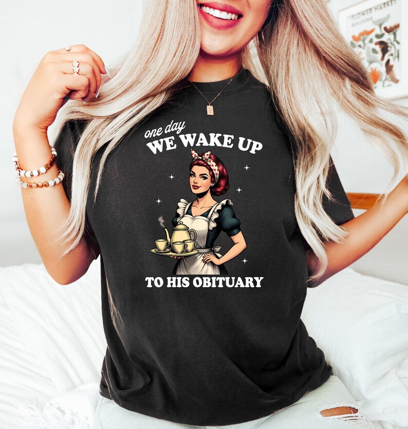 May include: Black t-shirt with a graphic of a woman in a maid outfit holding a teapot and teacups. The text on the shirt reads "one day we wake up to his obituary."