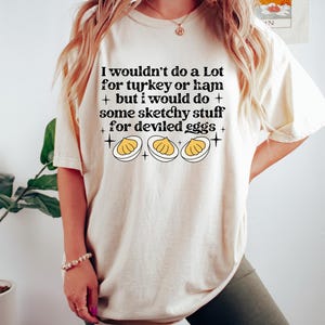 May include: Cream-colored t-shirt with the text "I wouldn't do a Lot for turkey or ham + but I would do + some sketchy stuff + for deviled eggs +" and a graphic of three deviled eggs.