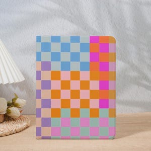 Op de afbeelding: Een rechthoekige hoes met een kleurrijk dambordpatroon. Het ontwerp bevat vierkanten in tinten blauw, oranje, roze en paars. De hoes staat rechtop op een houten oppervlak.