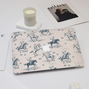 Peut inclure: Une coque d'ordinateur portable rose avec un motif répété de cowboys à cheval. Les cowboys sont dessinés en bleu foncé et tiennent des cordes. Le fond est de couleur rose clair.