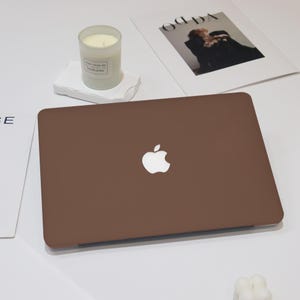 May include: A brown laptop computer with a white Apple logo on the lid. The laptop is on a white surface.