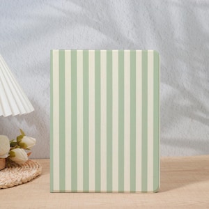 May include: A rectangular notebook with a vertical striped pattern in light green and off-white. The notebook is standing upright on a wooden surface. The background is a light gray wall.