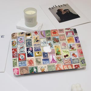 May include: A laptop computer with a colourful sticker design featuring a collage of vintage postage stamps from around the world. The stamps feature various images, including animals, flowers, landmarks, and text in different languages.